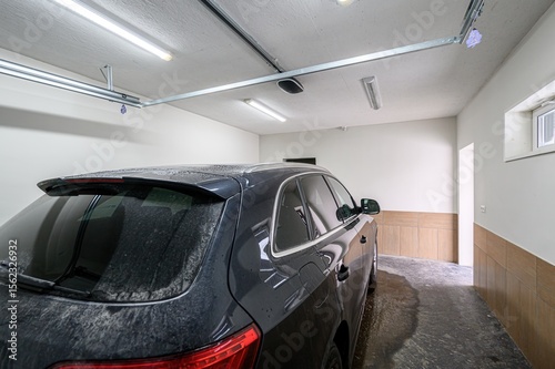 dark SUV is parked in a garage with white walls and ceiling, and tile accents. The floor is wet, and lights illuminate the space