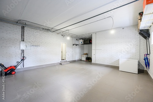 Clean, well-lit garage with white brick walls and gray tiled floor. A snowblower is near an electrical panel. A chest freezer sits against a wall