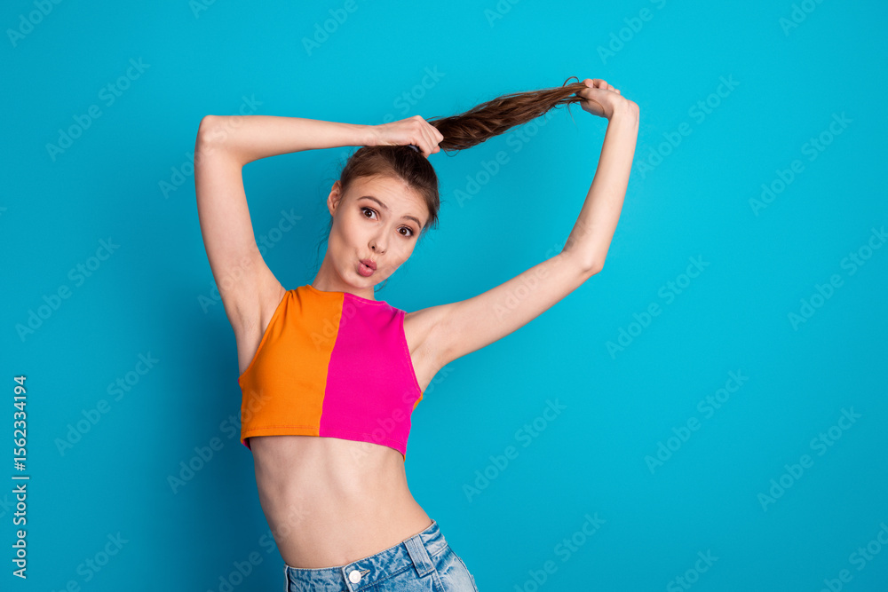 Fototapeta premium Bright young woman posing with playful expression against vivid blue backdrop, showcasing cheerful energy and fashionable attire.