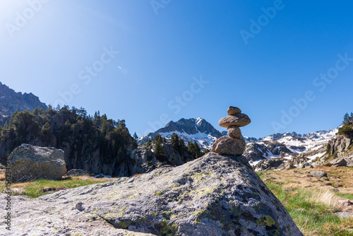 Stacked rocks on a boulder with snowy mountain peaks under a bright blue sky. Landmark. Trail marker. Stacked stones on a boulder with Pyrenean peaks and blue sky in the background. GR11