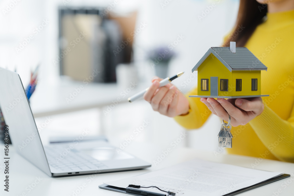 Fototapeta premium Home Showcase: A property expert displays a miniature house model in an office, symbolizing real estate prospects and the dreams of future homeowners.