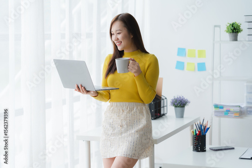 Modern Workspace Serenity: A focused individual finds comfort and efficiency in a bright, contemporary workspace. Holding laptop in one hand, sipping coffee with other hand.