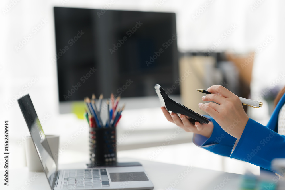 Fototapeta premium Businesswoman Analyzing Data: A closeup image of a businesswoman meticulously reviewing data on a calculator, demonstrating focus and attention to detail in a modern office setting.