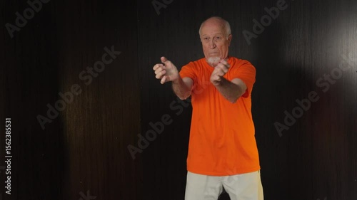 Old male athlete trains hand blocks in a standing position