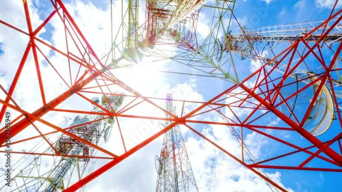 Looking up at a network of red and silver communication towers against sky