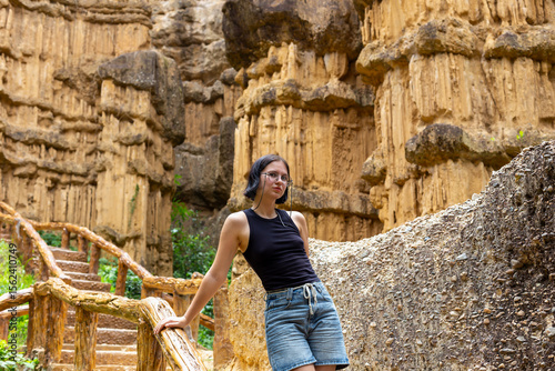 Young woman dressed in black tank top and denim shorts stands gracefully near unique rock formations, surrounded by lush greenery, showcasing beauty of natural landscapes and outdoor exploration
