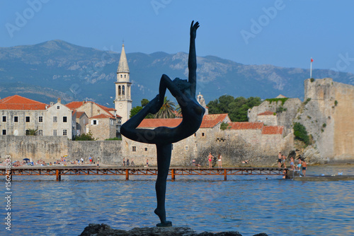 Iconic Ballerina Statue in Budva, Montenegro, with the Historic Old Town, Its Bell Tower, and Majestic Mountains Creating a Stunning Coastal Backdrop