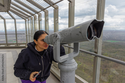 Billede på lærred A woman peers through large binoculars at an observation deck with panoramic win