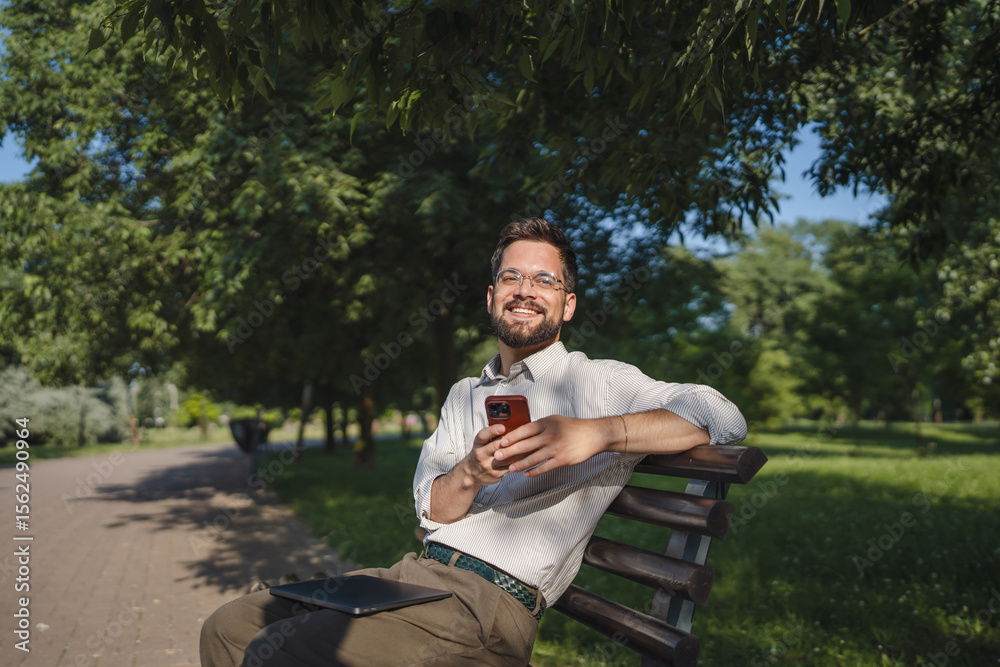 Obraz premium Adult man sit on bench in a public use mobile phone, leisure activity