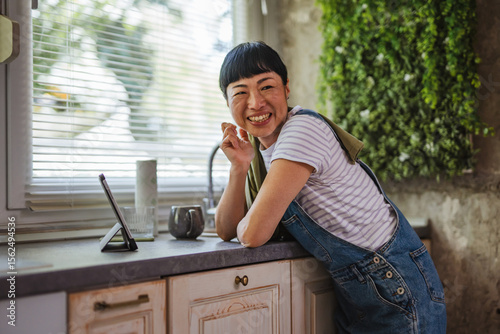 Tablou pe pânză Japanese woman watch tablet while take a break from wiping in kitchen