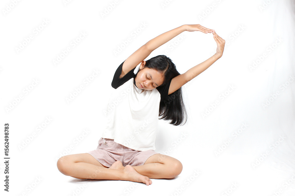 Fototapeta premium Young Asian woman doing yoga exercise sitting in lotus position while stretching her arms to the side isolated on white background