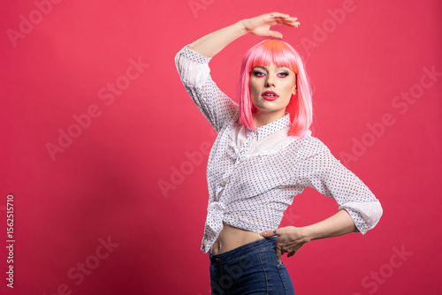 Gorgeous caucasian model with pink hair confidently striking a pose with one hand over head and other on waist. Beautiful young woman standing against isolated background, exuding self assurance.