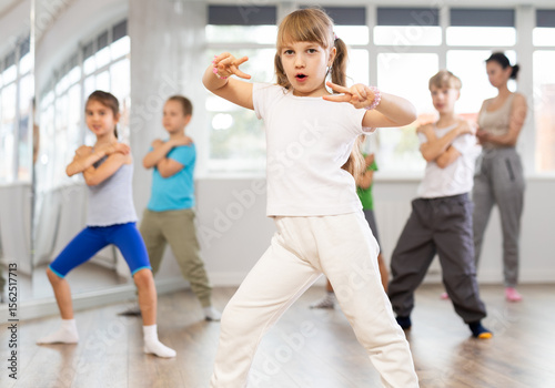During dance workshop, girl with team of young like-minded children learn to dance modern dances, doing movement with unrecognizable teacher. Studio school for amateur and professional dancers