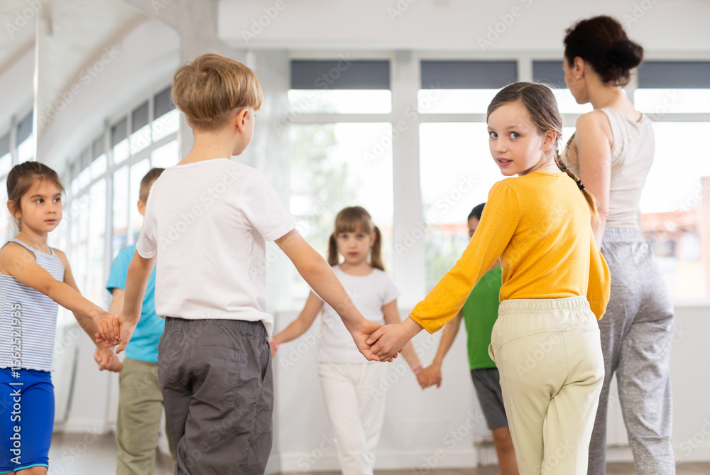 Fototapeta premium Boys and girls holding hands perform incendiary traditional roundelay folk dance during rehearsal in studio.