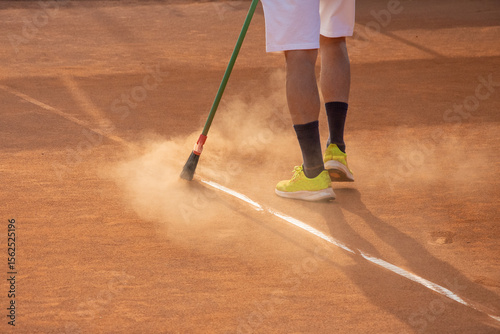 uomo che pulisce le righe del campo da tennis con scopa