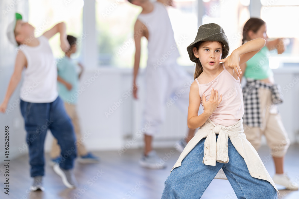 Obraz premium Focused preteen girl performing dynamic hip hop moves in group class for kids, led by skilled young male dance instructor in vibrant urban studio