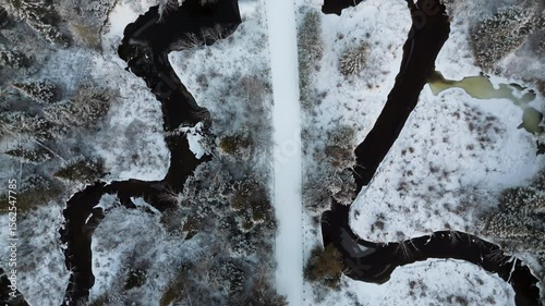 Aerial top-down view of snow-covered road, creek, and golden treetops in winter forest, lit by soft morning sunlight.