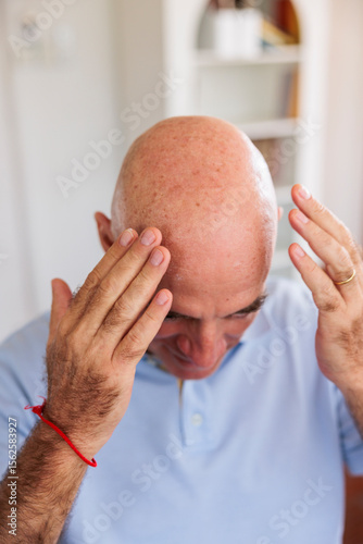 Man touching his bald head with both hands indoors
