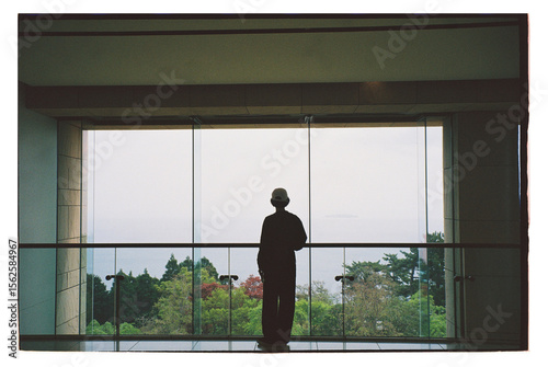 Person gazing out at a serene landscape from a modern building's