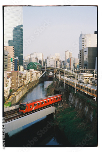 Urban landscape with vibrant red train crossing over a river 