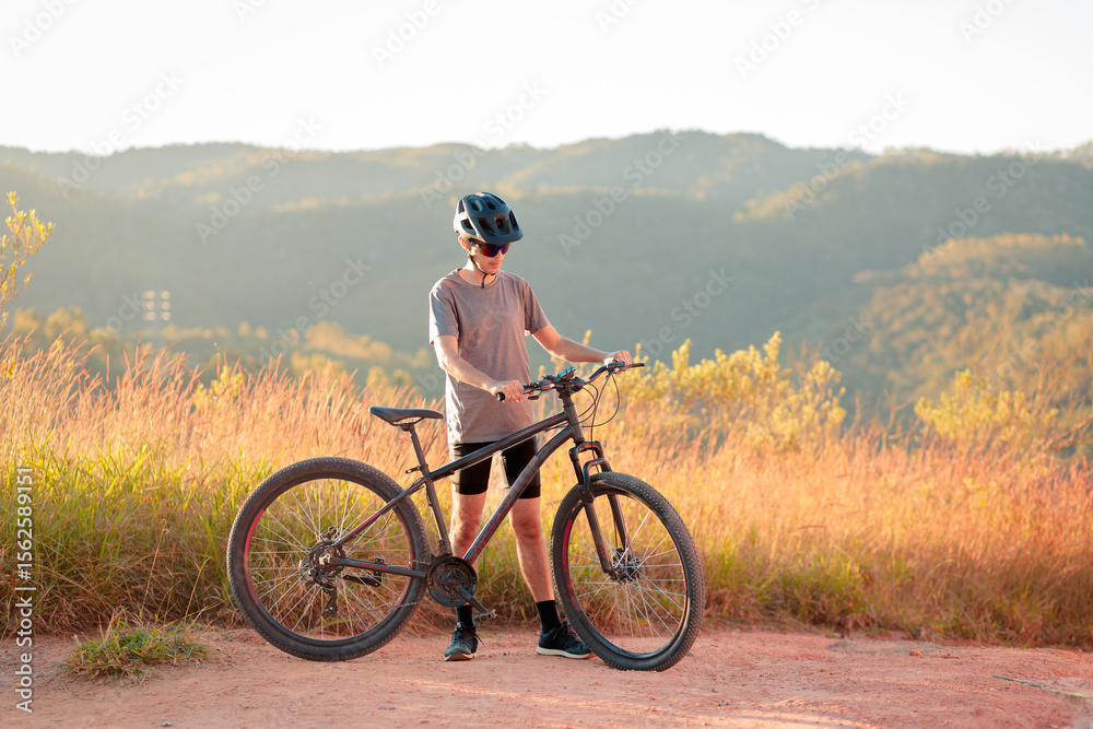 Naklejka premium Cyclist taking a quiet moment with his bike on a dirt trail. Outdoor activity promoting mindfulness, health, and connection with nature.
