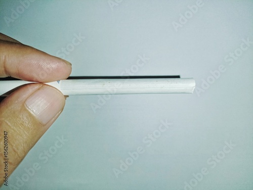 Schilderij op canvas A man holding an unlit white cigarette vertically against a plain light blue background