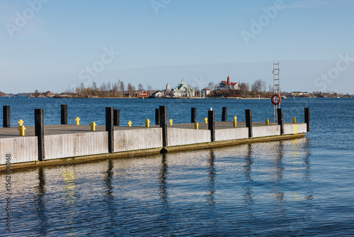 Wooden dock on calm water with island buildings in background photo