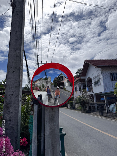 Cyclists reflected in traffic mirror under cloudy sky