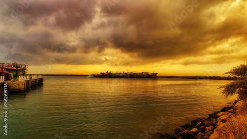 ships anchored at the pier at sunrise with clouds reflecting on the calm sea water