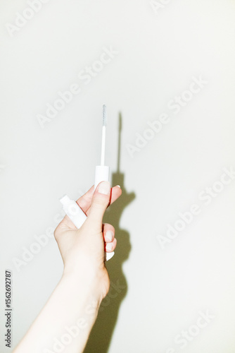 Hand holding cosmetic beauty lash serum treatment bottle & brush
