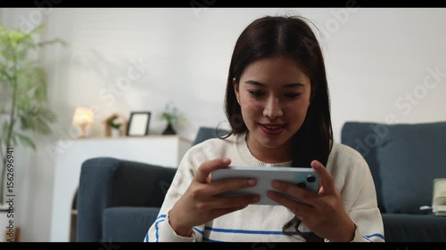 Woman is playing game on smartphone on vacation at home in living room, she is playing game with friend on smartphone, she is spending free time on vacation relaxing.