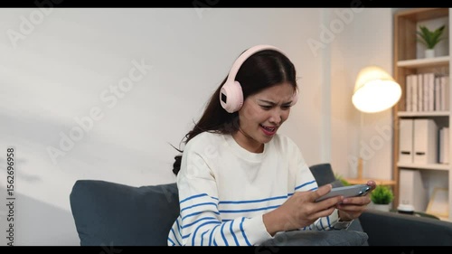 Woman is playing game on smartphone on vacation at home in living room, she is playing game with friend on smartphone, she is spending free time on vacation relaxing.