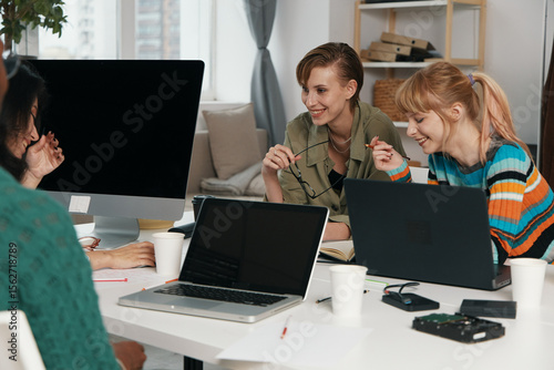 smiling young adult woman and friends socializing at workplace with laptops, business colleagues, Gen Z coworkers collaborating on work project