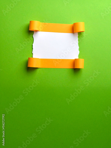 A single piece of torn white paper is horizontally placed on a vibrant green background, with its top and bottom edges curled back to reveal orange undersides, offering copy space for various uses.