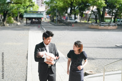 Fototapeta In June 2025, a young Japanese mother and father in their early twenties walk past the shrine's main hall, holding their one-month-old baby and honoring the traditional omiyamairi ceremony in Aichi