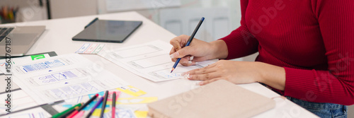 Asian women user interface designer sketching mobile app interface design for website layout design and digital project planning on paper at office