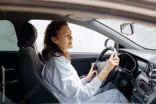 Happy calm woman driving in a car, holding a wheel, looking aside