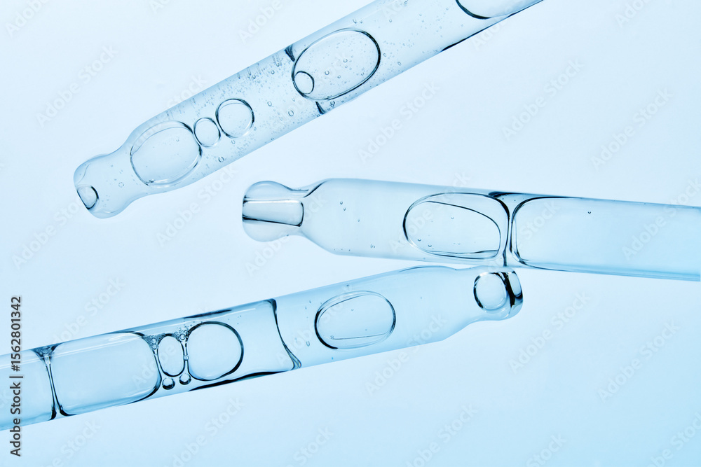 Several glass pipettes with liquid on gradient blue backdrop. 