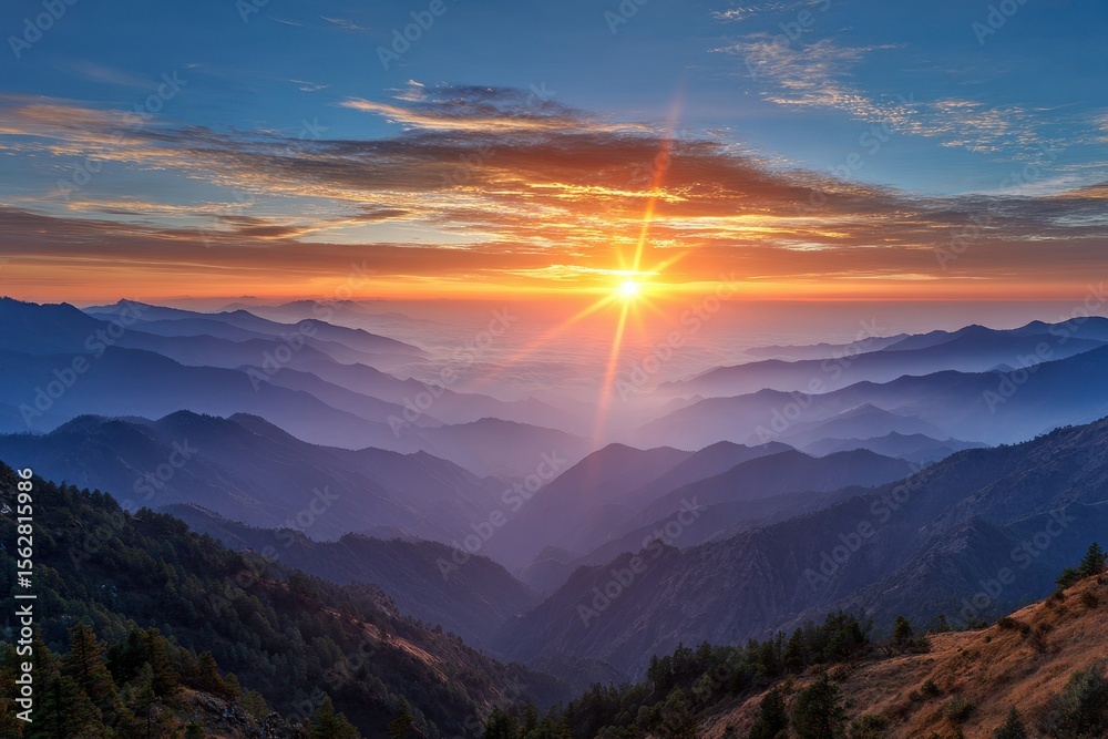 Obraz premium Vibrant sunrise over layered mountains with soft mist and colorful sky above them