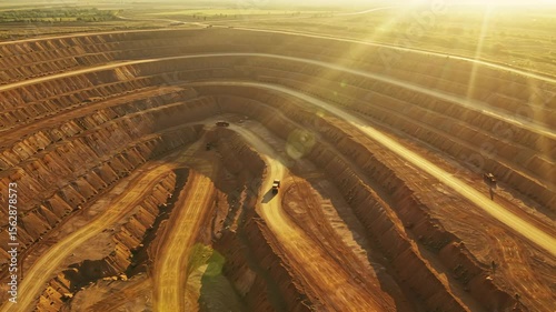 Aerial view of an expansive open-pit mining site at sunset with sun rays illuminating the dirt layers and machinery