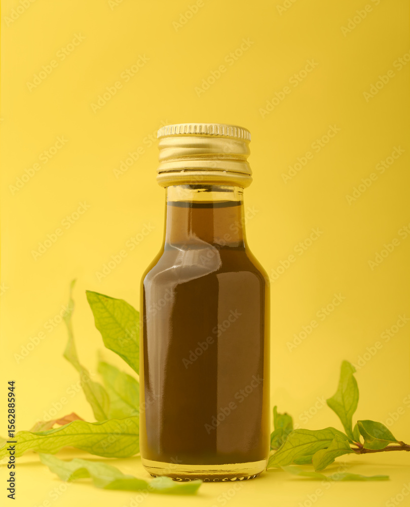 close-up of golden color herbal oil glass bottle with green herb leaves scattered, isolated yellow background with copy space, medicinal or ayurvedic liquid container mock-up template close-up of golden color herbal oil glass bottle with green herb leaves scattered, isolated yellow background with copy space, medicinal or ayurvedic liquid container mock-up template