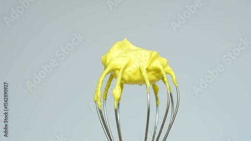 Whisk with yellow whipped cream from proteins close-up on gray background.
