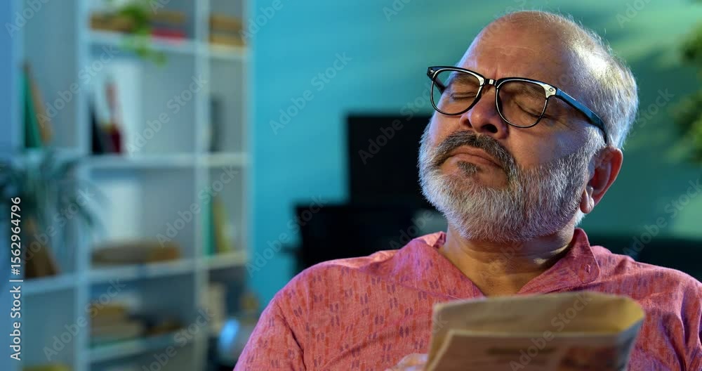 Indian man solving crossword puzzle with pencil while sitting at table, elderly Asian male reading newspaper, focused relaxed, enjoying peaceful morning brain exercise as part of daily routine