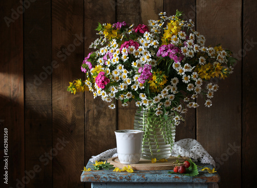 A lush bouquet of summer flowers in a transparent vase is placed on an old blue stool. still life with cute daisies, yellow verbena and pink carnations.