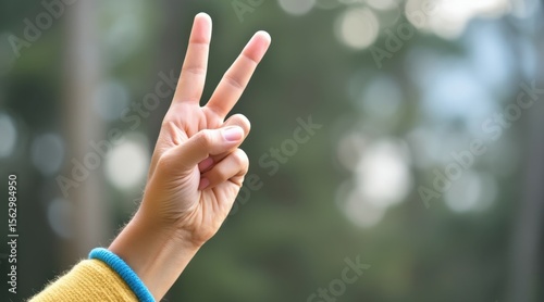 A close-up of a hand showing a peace sign with two fingers extended, against a blurred natural background.