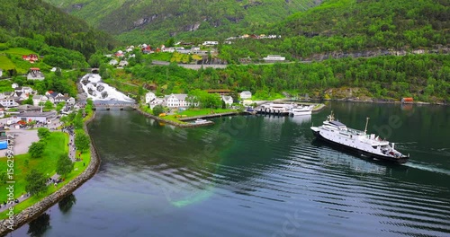 View on Hellesylt, a small village in the Sunnylvsfjord, Norway. Captured from a large cruise ship, the scene features a lush green landscape, a waterfall, and serene fjord waters.