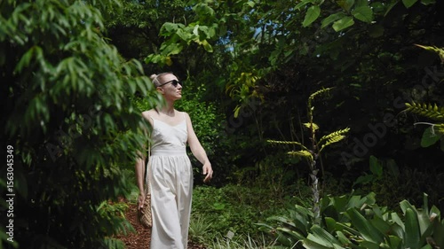 A stylish woman in a flowing white dress explores the Royal Botanic Garden in Sydney, surrounded by lush greenery and exotic plants.