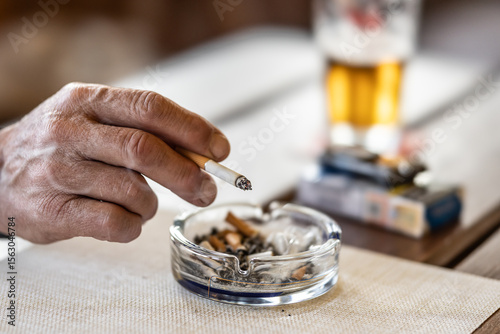 The hand of a smoking man or woman on a table led an ashtray with draft beer in a pub