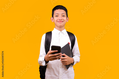 Cheerful Young Schoolboy Using Mobile Phone While Smiling Looking At Camera Over Yellow Background