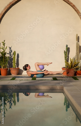 young pilates instructor doing exercice with lilac ball on mat near swimming pool